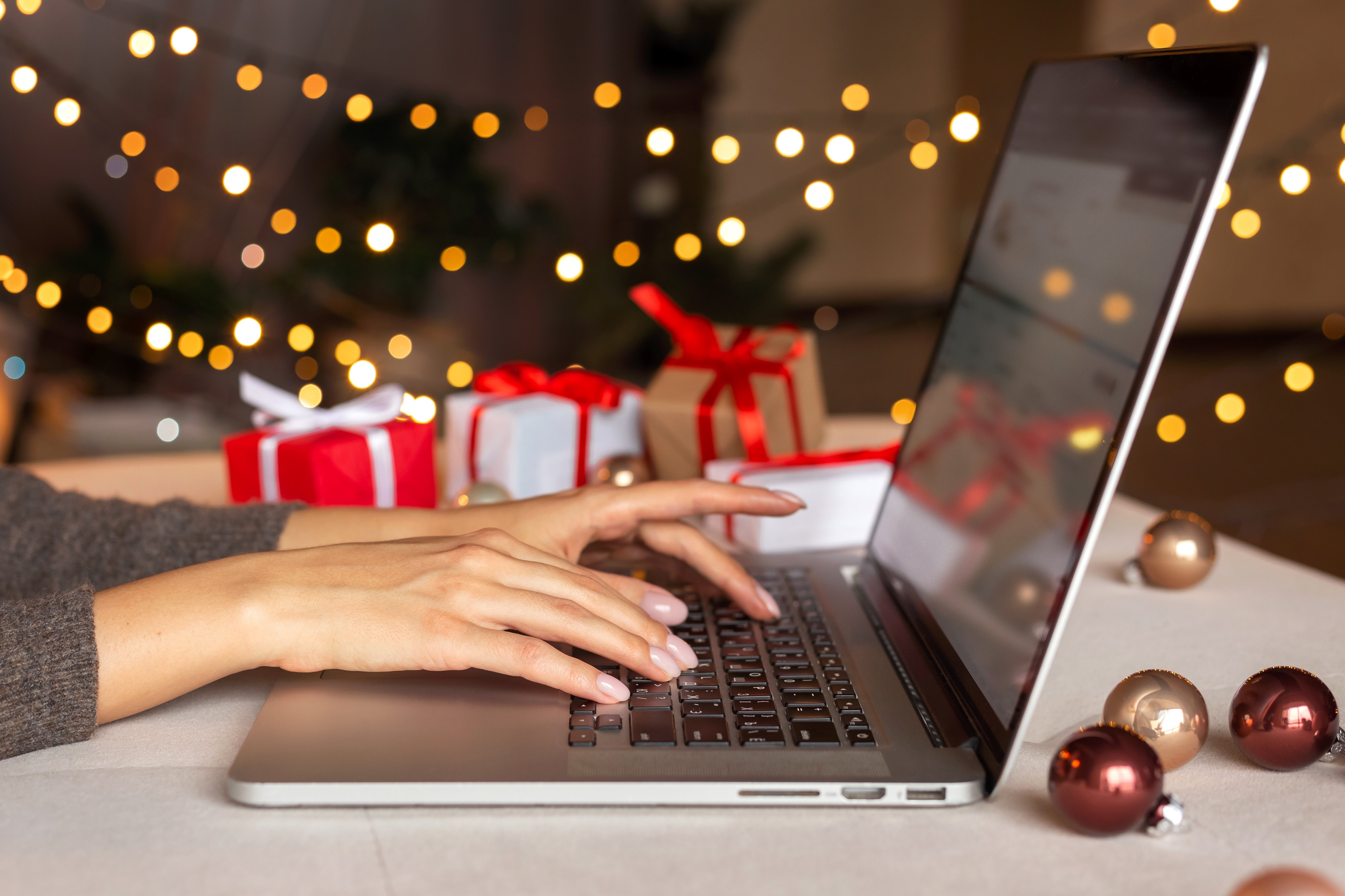 person typing on a laptop with a christmas tree and lights in the background to convey holiday shopping